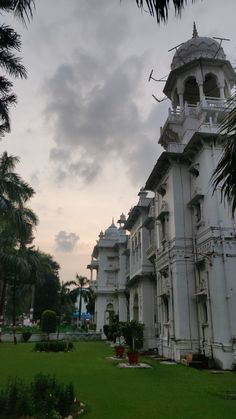 a large white building sitting on top of a lush green field next to palm trees