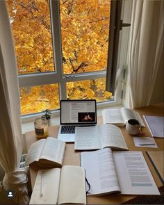 an open laptop computer sitting on top of a wooden desk next to books and papers