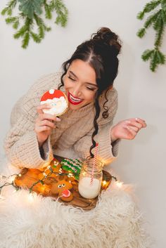 a woman is eating cookies and drinking milk while sitting on a furry surface with christmas decorations