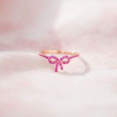 This elegant Pink Pavé Bow Ring is a testament to the timeless beauty of love. The ring glimmers with a subtle sheen, reflecting the warmth and radiance of love that shines within. Each detail of this ring is crafted with precision and care, from the smooth edges to the delicate bow design. When you gift this ring to your loved one, you are giving them a reminder of the beauty and strength of your love. It is a symbol of your commitment and devotion, a tangible expression of the intangible bond Gift Pink Ruby Halo Ring, Gift Pink Halo Ruby Ring, Delicate Pink Stackable Rings For Gifts, Pink Ruby Ring With Halo For Gift, Pink Ruby Halo Ring Perfect For Gift, Elegant Pink Gold Rings For Valentine's Day, Feminine Adjustable Wedding Rings, Dainty Pink Gold Rings For Gift, Dainty Pink Rings For Formal Occasions