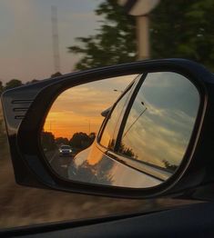 the rear view mirror of a car is shown as the sun sets in the distance