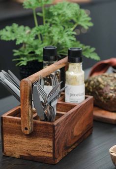 a wooden box with utensils in it on a table next to a potted plant