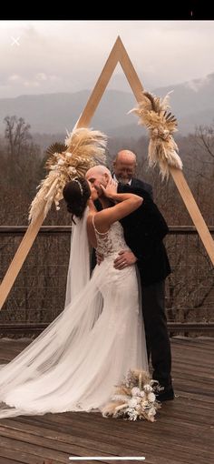 a bride and groom standing in front of a wooden structure with feathers on it's head