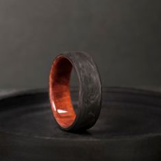 a wooden ring sitting on top of a black table next to a metal container with a red wood in it