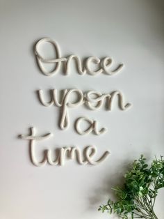 the words once upon as time are spelled in white yarn on a wall next to a potted plant