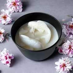 a black bowl filled with white liquid and fish in it next to some pink flowers