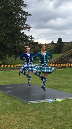 two young women in kilts are jumping on a trampoline at the park