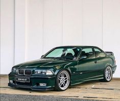 a green car parked in front of a white wall