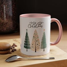 a pink and white coffee mug sitting on top of a wooden table next to a spoon