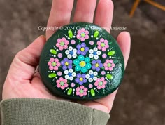 a hand holding a painted rock with flowers on it