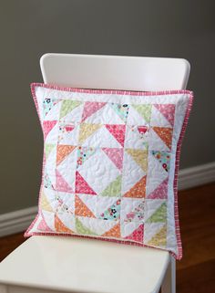 a white chair with a pink and green pillow on it