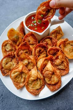 a person dipping sauce on some appetizers in a white plate with other food items