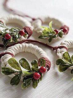 three white wreaths with red berries and green leaves on them sitting on a table