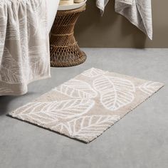 a white rug with leaves on it next to a basket and towel hanging from a rack