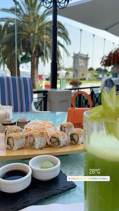 sushi and drinks are on the table at an outdoor restaurant with palm trees in the background