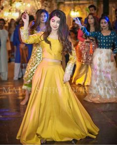 a woman in a yellow dress dancing on the dance floor with other people around her