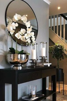 a black console table with flowers and candles on it in front of a staircase area