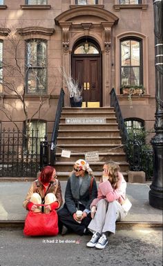 three people sitting on the sidewalk in front of a building