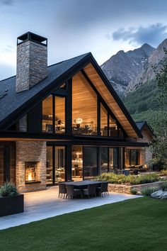 a large house with an outdoor dining area in front of it and mountains behind it