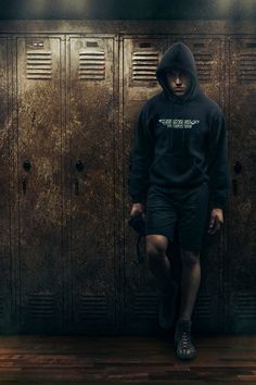 a man standing in front of lockers wearing a black hoodie and sweat shorts