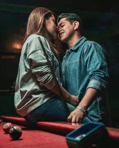 a man and woman sitting next to each other on top of a red pool table