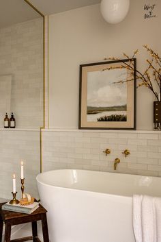 a white bath tub sitting under a painting next to a wooden table with candles on it