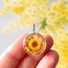 a hand holding a glass pendant with a yellow sunflower on it's side