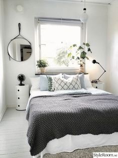 a bedroom with white walls, black and white bedding and plants on the window sill