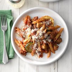 two plates with pasta and sauce on them next to a fork, knife and napkin