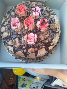 a chocolate cake with pink flowers on top in a box next to a woman's hand