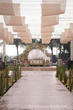 an outdoor ceremony setup with white draping and flowers on the aisle, surrounded by palm trees