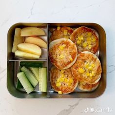 a metal container filled with food on top of a white counter next to cucumbers and apples