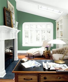 a living room with green walls and white trim on the fireplace mantel, chair, coffee table, and bookshelf