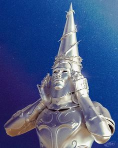 a silver statue with a pointed hat on it's head and hands behind her head