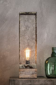 a green glass vase sitting on top of a wooden table next to a light bulb