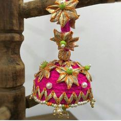 a pink and gold decorated bell hanging from a wooden pole with beads on it's sides