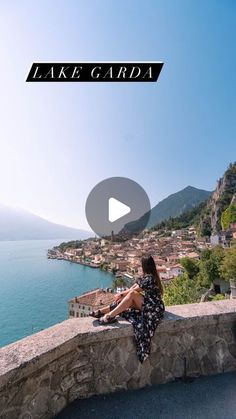 a woman sitting on top of a stone wall next to the ocean and town below