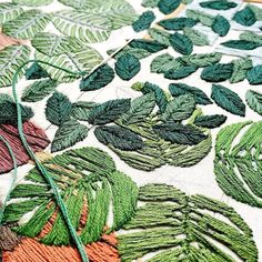 some green and orange leaves on a white table cloth with thread in the middle that has been stitched together