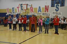 children holding up signs in front of an audience at a school gym with people standing on the sidelines