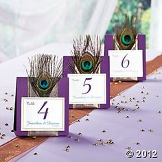 the table numbers are decorated with purple and white peacock feathers as well as silver confetti