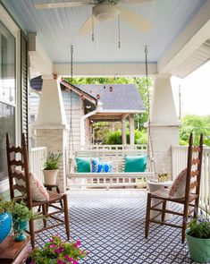 a porch with two rocking chairs on the front porch and blue pillows hanging from the ceiling