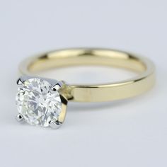 a yellow gold engagement ring with a round brilliant cut diamond in the center, on a white background