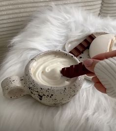 a person is dipping some kind of chocolate into a white cup with cream on it