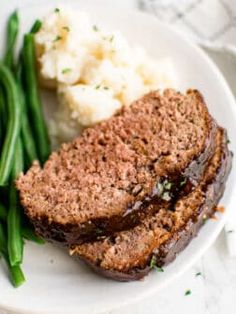 two slices of meatloaf on a plate with green beans and mashed potatoes