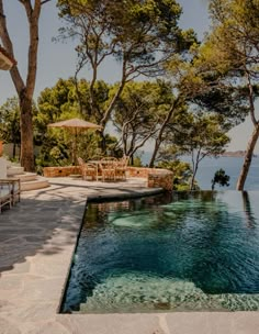 an outdoor swimming pool surrounded by trees and chairs with umbrellas on the side, overlooking the water