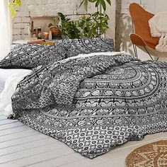 a bed with black and white comforter in a room next to a chair, rug and potted plant