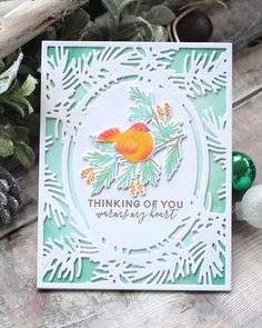 a card with a bird on it sitting next to some christmas balls and pine cones