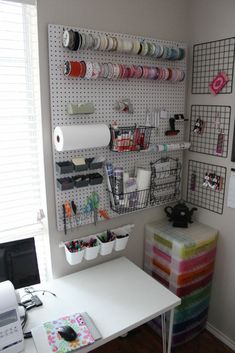 a white desk topped with lots of crafting supplies next to a wall mounted pegboard