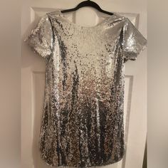 Do Not Miss Out On This Snag! You Will Stand Out And This Dress Is For Sure To Get Many Compliments. This T-Shirt Dress Has So Much Class And Edge To It! Can Dress It Up Or Down. Has A Low Cut Back And Some Cute Cut Outs In The Shoulder! Never Worn. I Love This Dress And Wish It Fit Me The Correct Way! Size Medium Still With Tags! Metallic Sequin Holiday Dress With Shimmer, Metallic Sequin Shimmer Dress For Holidays, Metallic Shimmer Sequin Dress For Holidays, Metallic Shimmer Sequin Holiday Dress, Metallic Sequin Dress With Glitter For Party Season, Metallic Glitter Sequin Dress For Party Season, Cocktail Short Sleeve Sequin Dress With Contrast Sequin, Glamorous Short Sleeve Sequin Dress With Contrast Sequins, Silver Embellished Sequin Fabric For Night Out