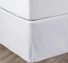 a bed with white sheets on top of it and wood flooring in the background